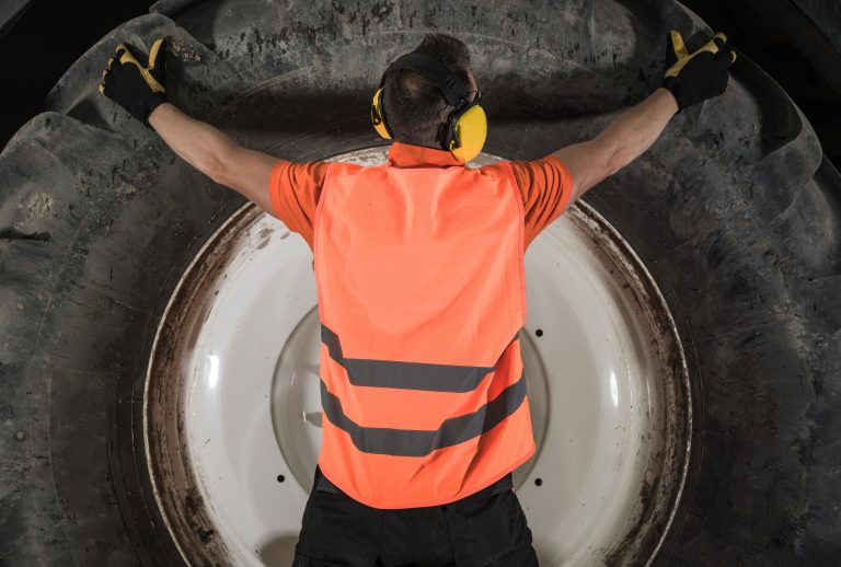 Replacing Heavy Equipment Tire Concept. Caucasian Machinery Operator and the Heavy Duty Wheel.